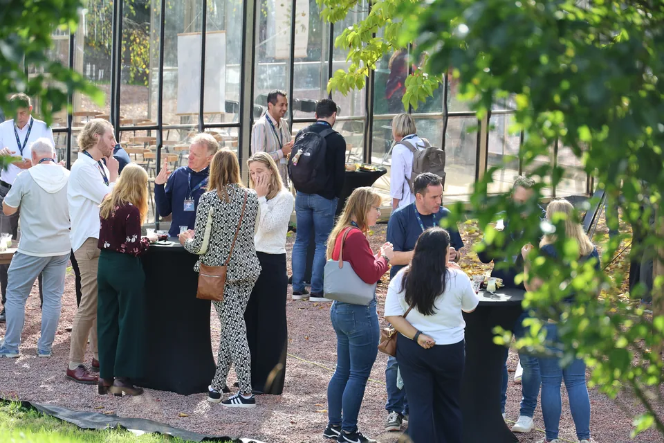 Bezoekers in gesprek bij de statafels, buiten tussen het groen