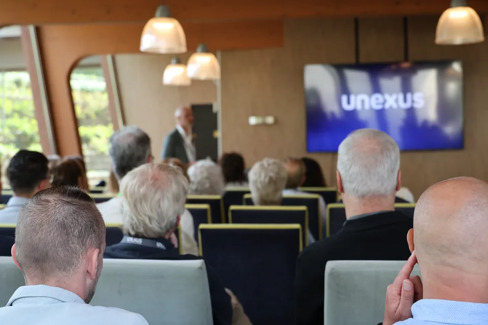 De zaal kijkt naar het scherm waarop de nieuwe naam van Unexus verschijnt