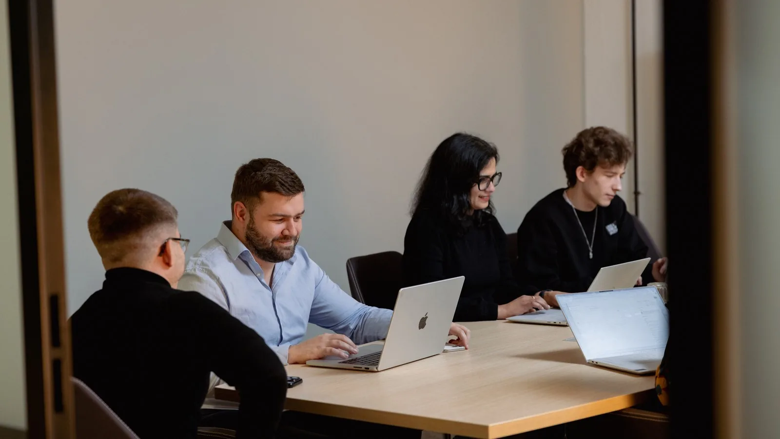 Four colleagues with laptops around a table in a meeting